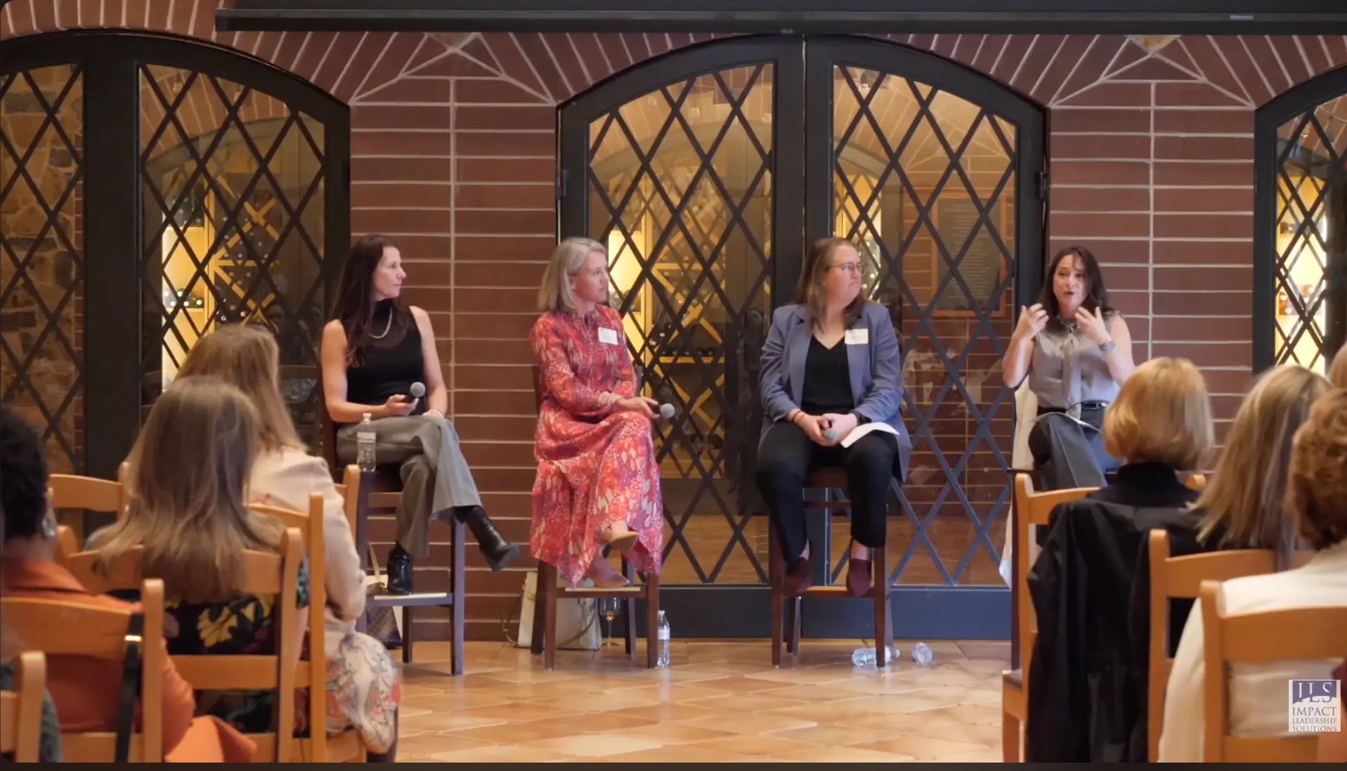 Four women seated on tall stools speaking into microphones during an Executive Voices panel, with attendees seated in front of them